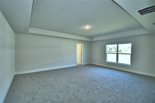 carpeted empty room featuring baseboards, a tray ceiling, and visible vents