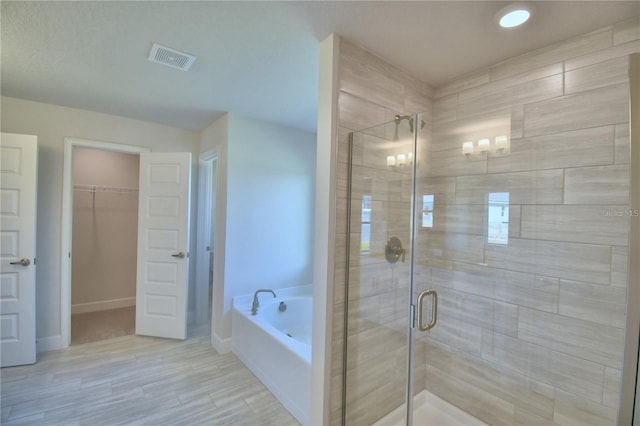 bathroom with a spacious closet, a shower stall, a garden tub, and visible vents