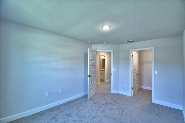 unfurnished bedroom with a spacious closet, carpet, baseboards, visible vents, and a closet