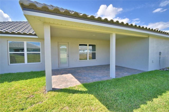 doorway to property with a tiled roof, stucco siding, a yard, and a patio area