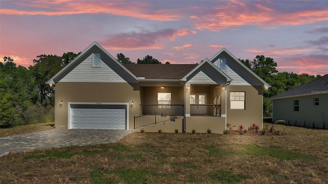 view of front facade featuring driveway, covered porch, an attached garage, stucco siding, and a front lawn