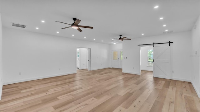 unfurnished living room with a barn door, visible vents, recessed lighting, light wood finished floors, and a ceiling fan