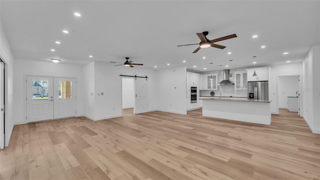 unfurnished living room featuring a ceiling fan, recessed lighting, light wood finished floors, and a barn door