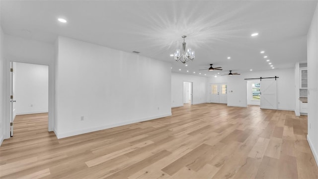 unfurnished living room featuring ceiling fan with notable chandelier, a barn door, light wood-type flooring, recessed lighting, and baseboards
