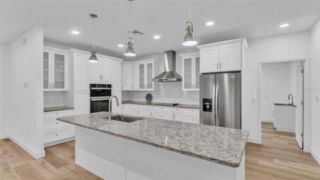 kitchen featuring a sink, wall chimney exhaust hood, stainless steel appliances, light wood-type flooring, and decorative backsplash