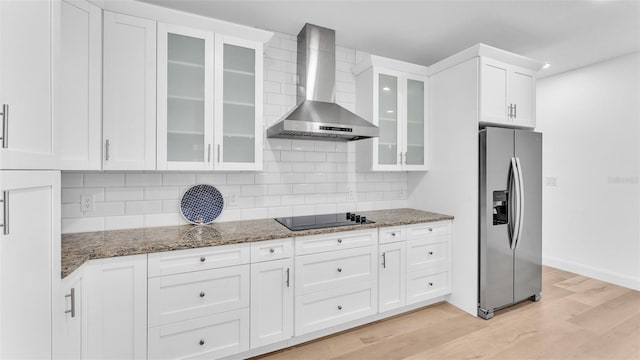 kitchen with wall chimney range hood, black electric stovetop, dark stone countertops, light wood finished floors, and stainless steel fridge with ice dispenser
