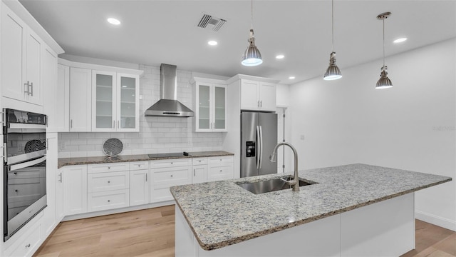 kitchen featuring a sink, visible vents, wall chimney exhaust hood, light wood-style flooring, and appliances with stainless steel finishes