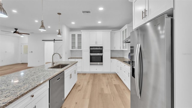 kitchen with light wood-style flooring, a barn door, a sink, tasteful backsplash, and appliances with stainless steel finishes