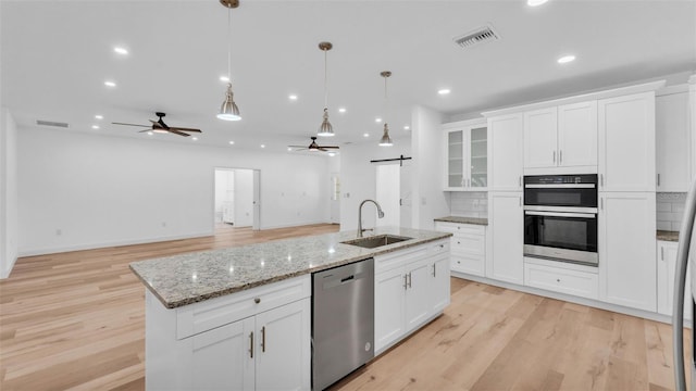 kitchen with a sink, stainless steel appliances, a barn door, ceiling fan, and white cabinetry