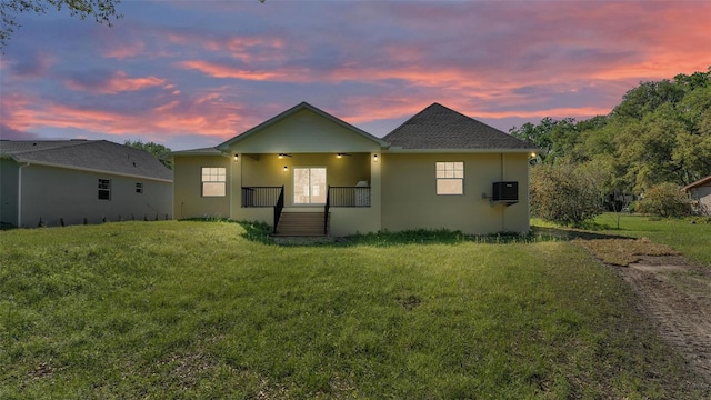 back of house at dusk featuring stucco siding, a lawn, and a porch