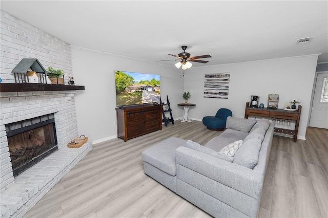 living room with visible vents, ornamental molding, light wood-style flooring, a brick fireplace, and ceiling fan