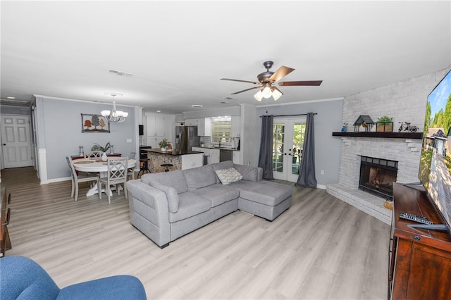 living area with light wood-type flooring, visible vents, ceiling fan with notable chandelier, crown molding, and a fireplace
