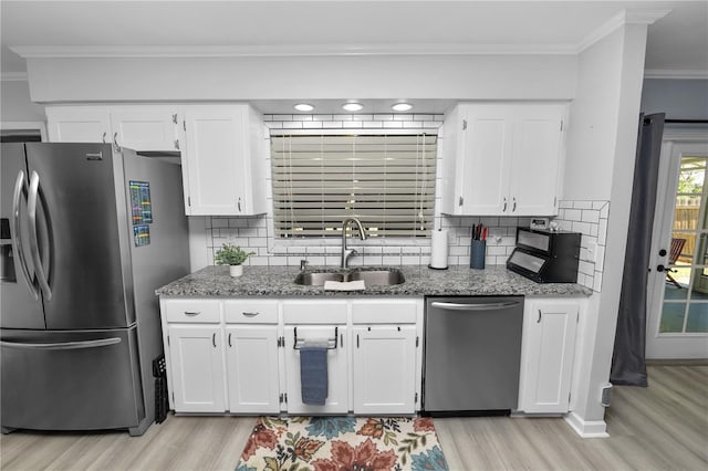 kitchen with light wood finished floors, a sink, decorative backsplash, crown molding, and appliances with stainless steel finishes