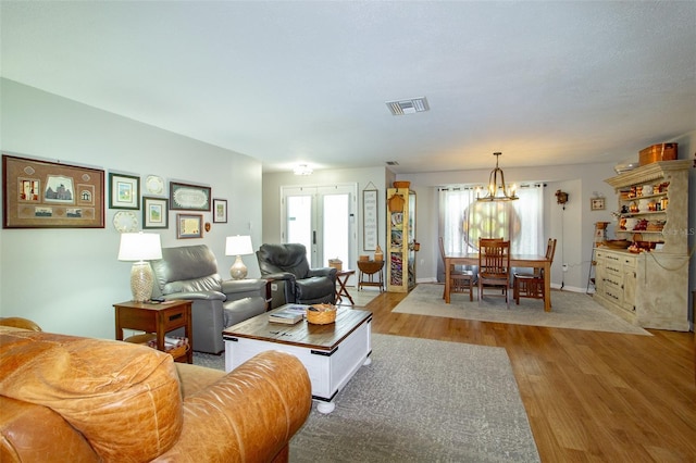 living area with baseboards, visible vents, a chandelier, and wood finished floors