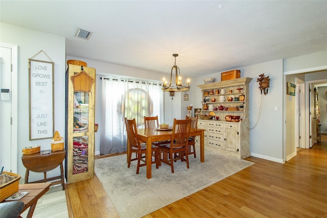 dining area featuring baseboards, light wood-style floors, a chandelier, and visible vents