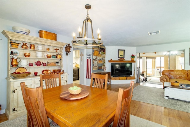 dining space with light wood finished floors, visible vents, a fireplace, and a chandelier