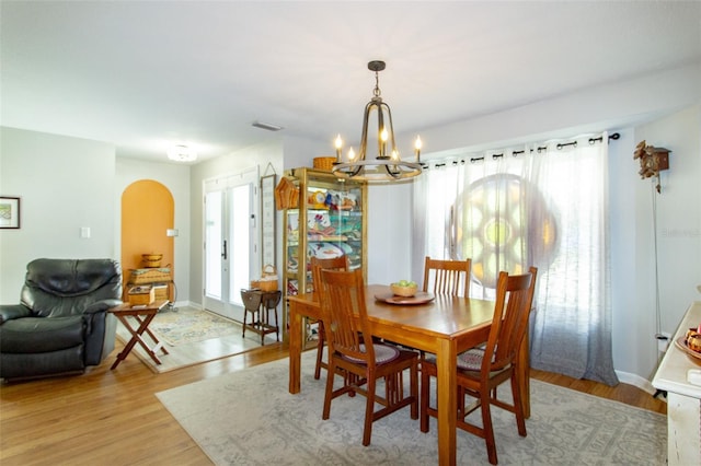 dining room with visible vents, baseboards, arched walkways, light wood-style floors, and an inviting chandelier