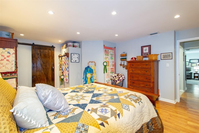 bedroom with light wood finished floors, a barn door, baseboards, visible vents, and recessed lighting
