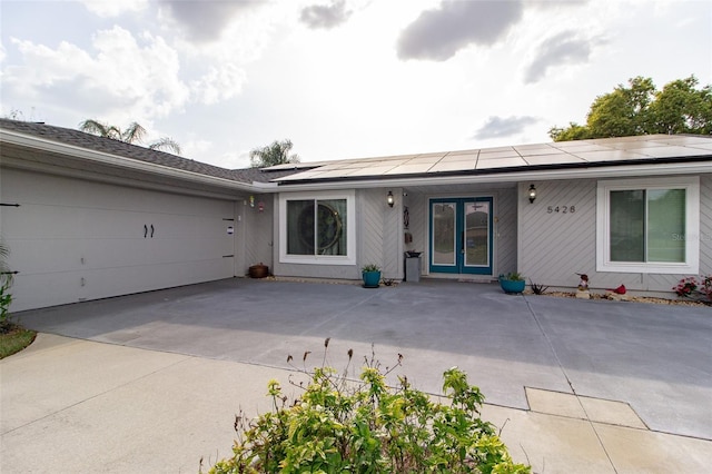 view of front of property featuring driveway, a garage, french doors, and solar panels