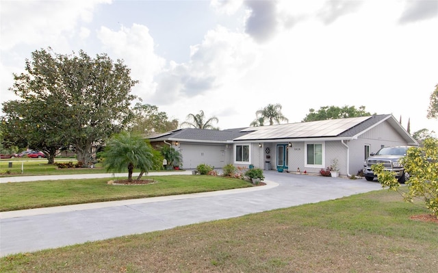 ranch-style home with curved driveway, solar panels, and a front lawn