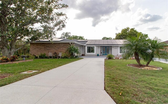 ranch-style home with a front lawn, brick siding, driveway, and solar panels