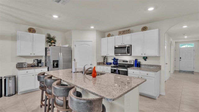 kitchen with a sink, a center island with sink, stainless steel appliances, visible vents, and arched walkways