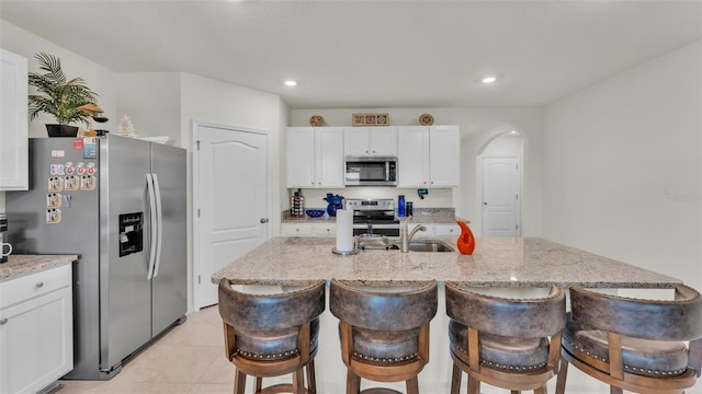 kitchen featuring a breakfast bar area, stainless steel appliances, light stone countertops, white cabinets, and a kitchen island with sink