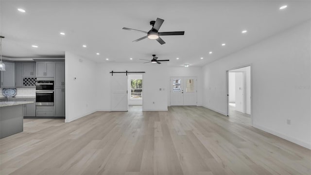 unfurnished living room with a barn door, recessed lighting, light wood finished floors, a ceiling fan, and baseboards