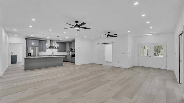 unfurnished living room with a barn door, recessed lighting, a ceiling fan, baseboards, and light wood-style floors