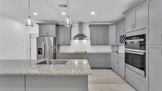kitchen with double wall oven, gray cabinetry, stainless steel fridge, and wall chimney exhaust hood