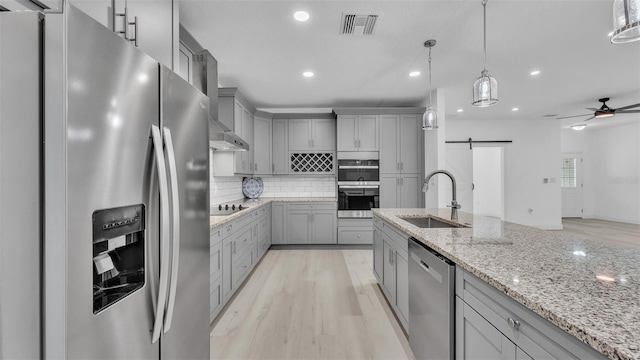 kitchen featuring gray cabinetry, a barn door, appliances with stainless steel finishes, and a sink
