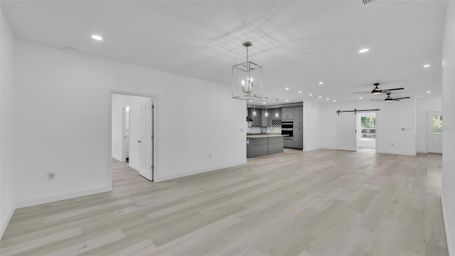unfurnished living room with baseboards, recessed lighting, light wood-style flooring, and a barn door