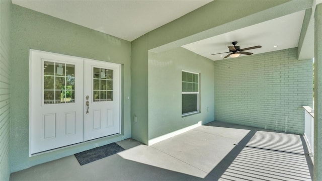 entrance to property with stucco siding, brick siding, and ceiling fan