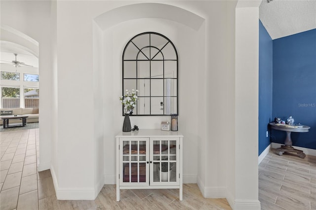 interior space featuring baseboards, arched walkways, ceiling fan, and wood finish floors