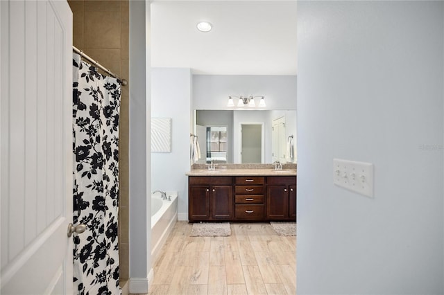 bathroom with double vanity, wood finished floors, a shower with curtain, a sink, and a garden tub