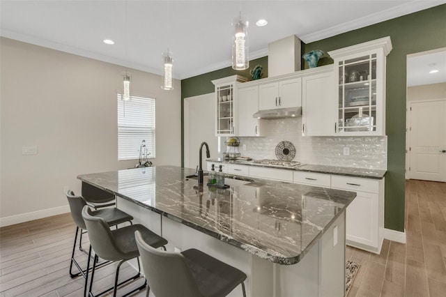 kitchen featuring a sink, light wood-type flooring, baseboards, stainless steel gas stovetop, and under cabinet range hood