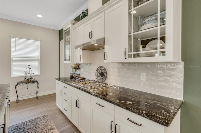 kitchen with white cabinets, stainless steel gas cooktop, dark stone counters, decorative backsplash, and under cabinet range hood