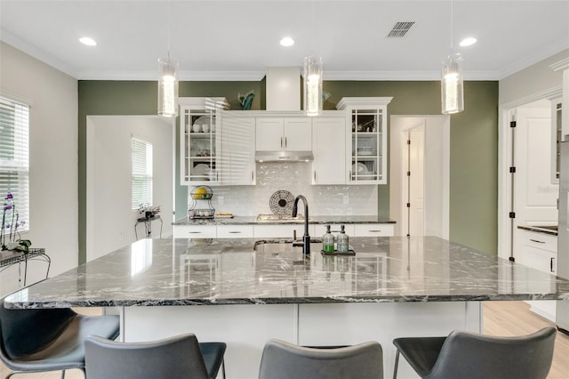 kitchen featuring white cabinets, decorative backsplash, under cabinet range hood, and a kitchen bar
