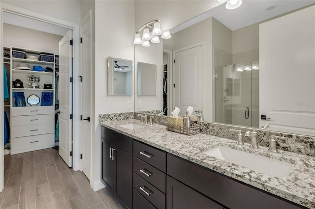 full bathroom with double vanity, a shower stall, a spacious closet, and a sink