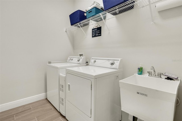 clothes washing area with laundry area, a sink, light wood-style floors, baseboards, and washer and dryer
