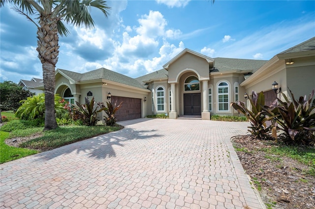single story home with stucco siding, decorative driveway, an attached garage, and roof with shingles