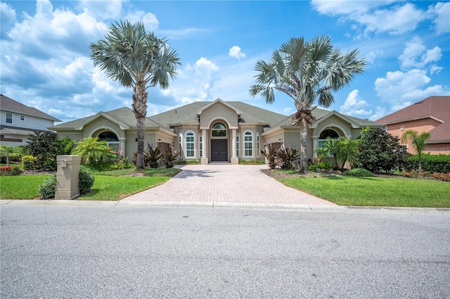 single story home with decorative driveway, a front lawn, an attached garage, and stucco siding