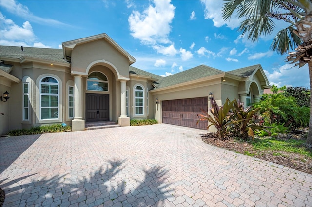 mediterranean / spanish home with stucco siding, an attached garage, decorative driveway, and roof with shingles