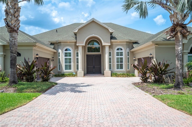 view of front of home with an attached garage, decorative driveway, stucco siding, and roof with shingles