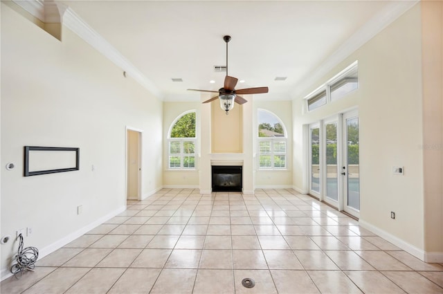 unfurnished living room with healthy amount of natural light, light tile patterned flooring, a ceiling fan, a glass covered fireplace, and crown molding