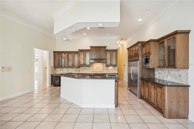 kitchen featuring built in appliances, dark countertops, light tile patterned flooring, an island with sink, and crown molding