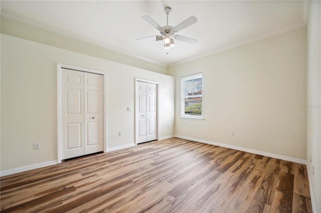 unfurnished bedroom with two closets, light wood finished floors, ornamental molding, baseboards, and ceiling fan