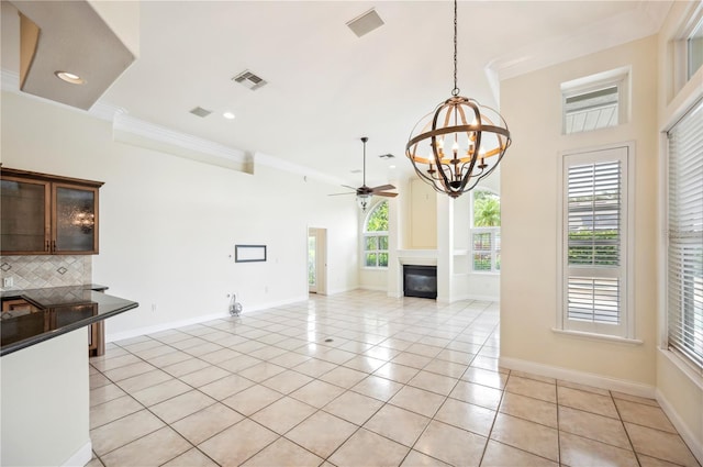 unfurnished dining area with a chandelier, light tile patterned flooring, ornamental molding, baseboards, and a glass covered fireplace