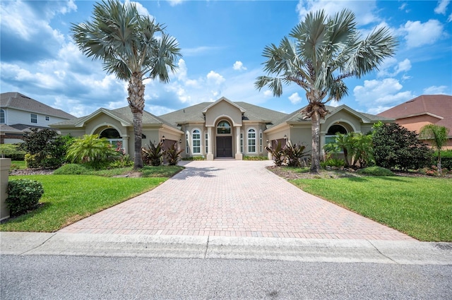 view of front of property with an attached garage, decorative driveway, stucco siding, and a front lawn