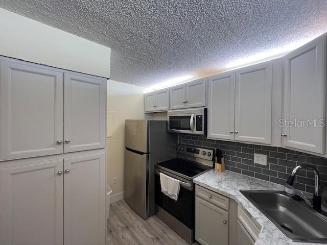 kitchen featuring a sink, light wood-type flooring, decorative backsplash, a textured ceiling, and appliances with stainless steel finishes